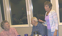 Woman stands at a table with several people chatting